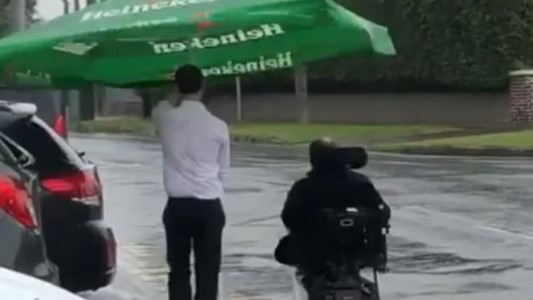 Un mozo usa una sombrilla para proteger a un hombre en silla de ruedas